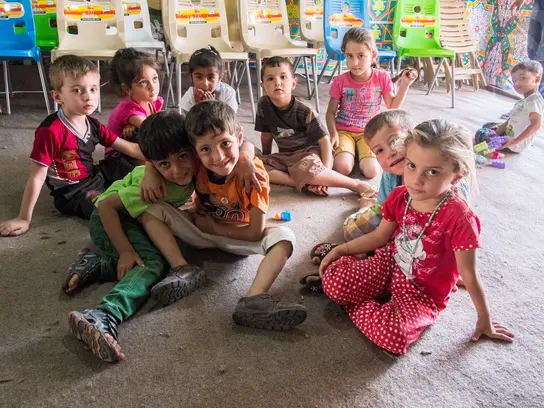 EIne Gruppe irakischer Schulkinder sitzt auf dem Boden des Klassenzimmers und schaut in die Kamera. Einige lächeln.