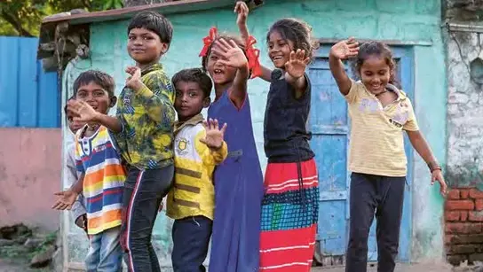 6 Kinder in bunter Kleidung stehen auf einer Steinmauer und winken in die Kamera.