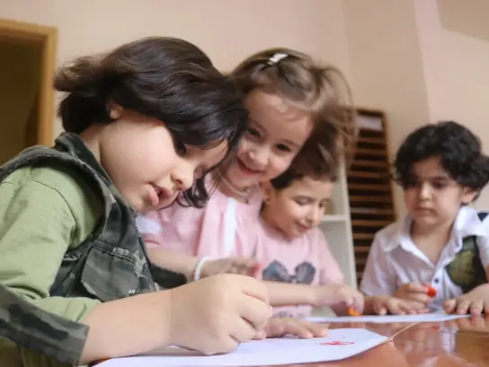 Vier Kinder sitzen lachend an enem Tisch und malen.