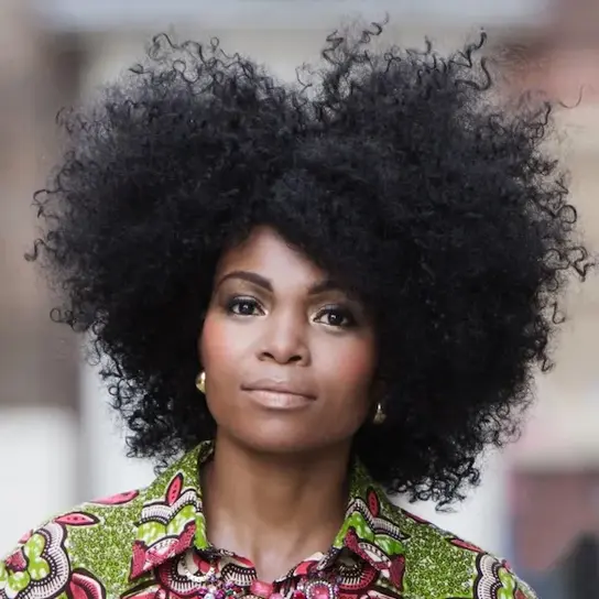 | © Simon Fowler Portrait von Pumeza Matshikiza, einer schlanken Schwarzen Frau mit lockigem, schwarzen Haar in einem lockeren Afro. Sie trägt eine farbenfroh gemusterte Bluse und schaut freundlich in die Kamera.