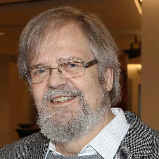 Portrait von Lutz Beisel, ein Mann mit grauem Haar und Kinnbart. Er trägt eine schmale, rechteckige Brille und lächelt in die Kamera.