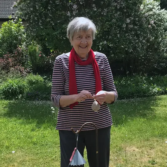 Frau Lorenzen, eine schlanke Frau mit kurzem grauem Haar steht im Grünen und hält einen Meisenknödel in den Händen.