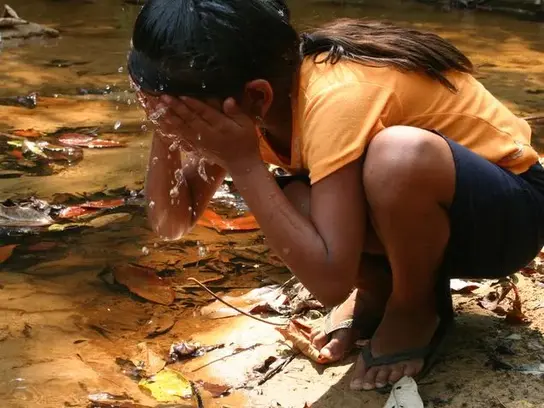 Ein Kind wäscht sich sein Gesicht im Fluss.