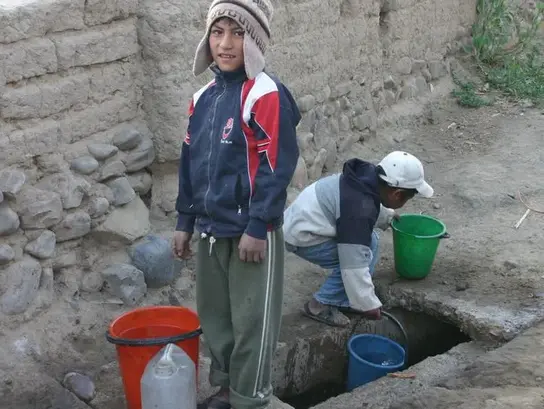 Zwei Kinder schöpfen mit Plastikgefäßen Wasser aus dem Boden.