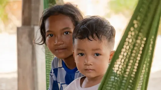 Zwei südost-asiatische Kinder sitzen in einer grünen Hängematte und gucken in die Kamera.