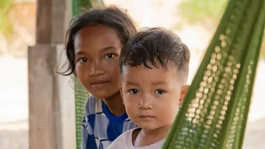 Zwei südost-asiatische Kinder sitzen in einer grünen Hängematte und gucken in die Kamera.