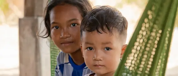 Zwei südost-asiatische Kinder sitzen in einer grünen Hängematte und gucken in die Kamera.